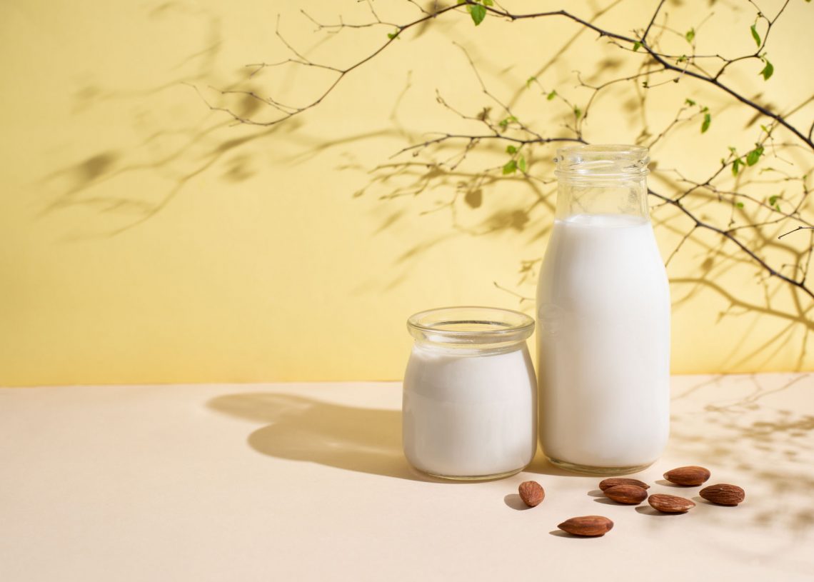 Jar and bottle with almond milk and almonds on a yellow background in sunlight, vegetarian milk, healthy food concept.